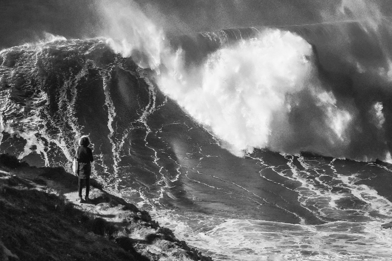 A spectator on the cliffs watching a huge wave break at Nazaré