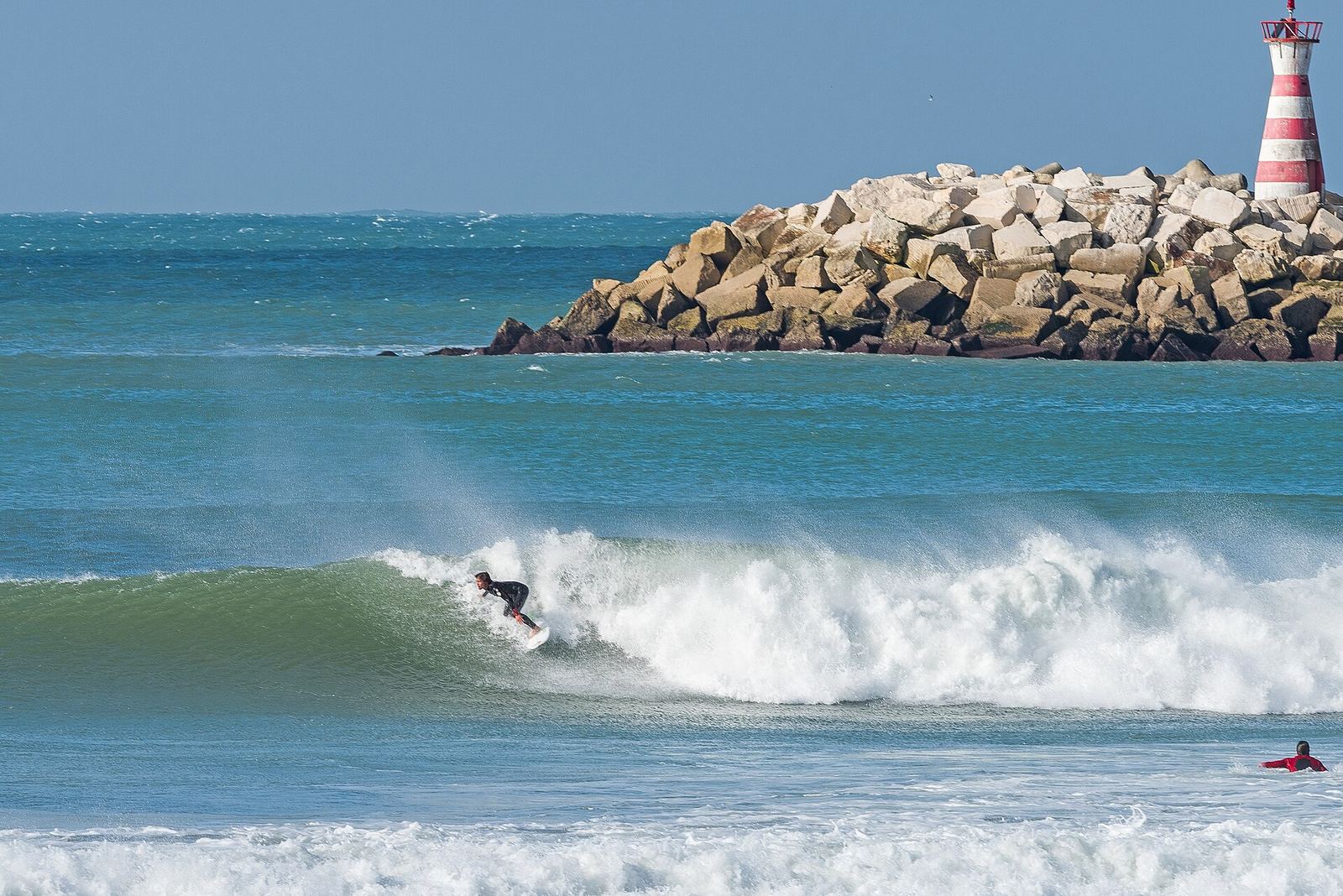 Surfer riding a wave by the Peniche harbour lighthouse